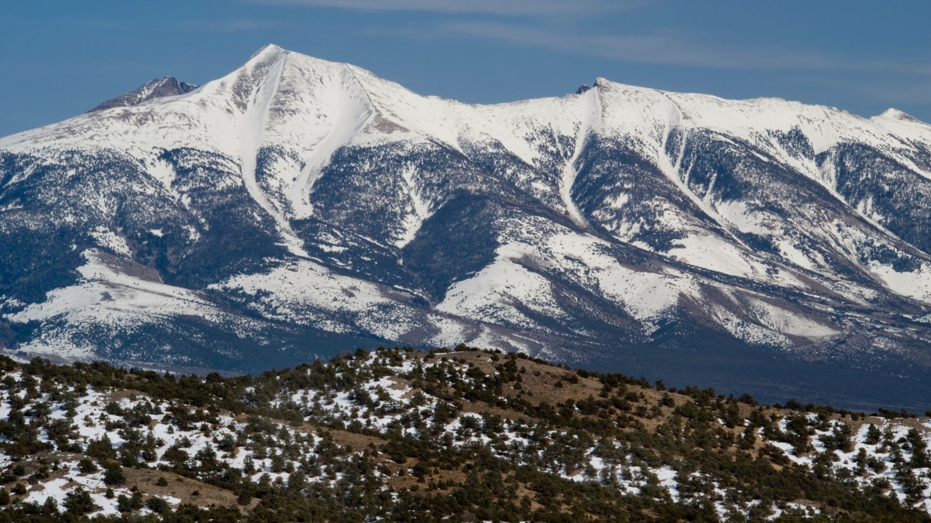 A scenic view of snow-capped mountains and foothills under a blue sky.