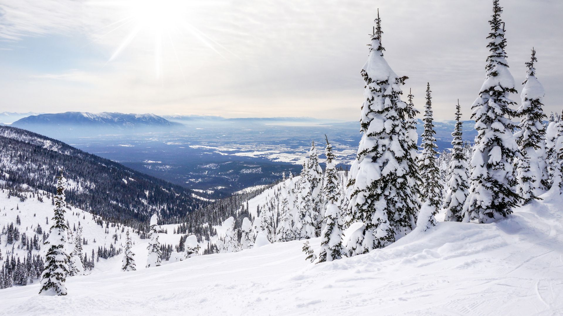A view from a snowy mountain ski slope looking down into a wide, snow-covered valley surrounded by distant mountains under a bright, sunny sky in Whitefish, Montana.
Would you like inf