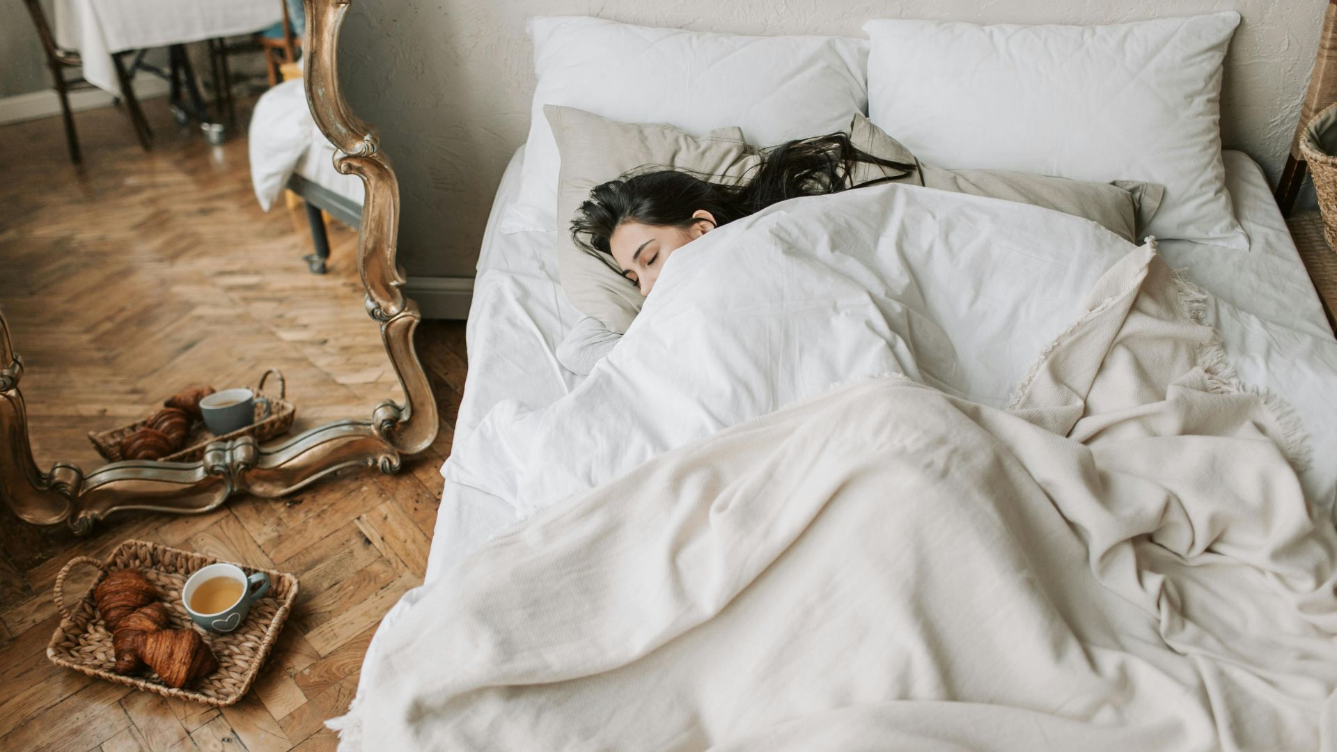 A woman sleeping comfortably in a bed with breakfast pastries and coffee on a tray nearby.