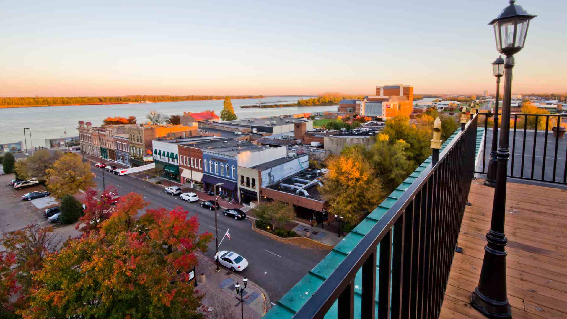 An aerial view of the downtown area of Paducah, Kentucky, with several multi-story buildings and autumn trees lining the streets leading toward a wide river, bordered by a floodwall in the background.
